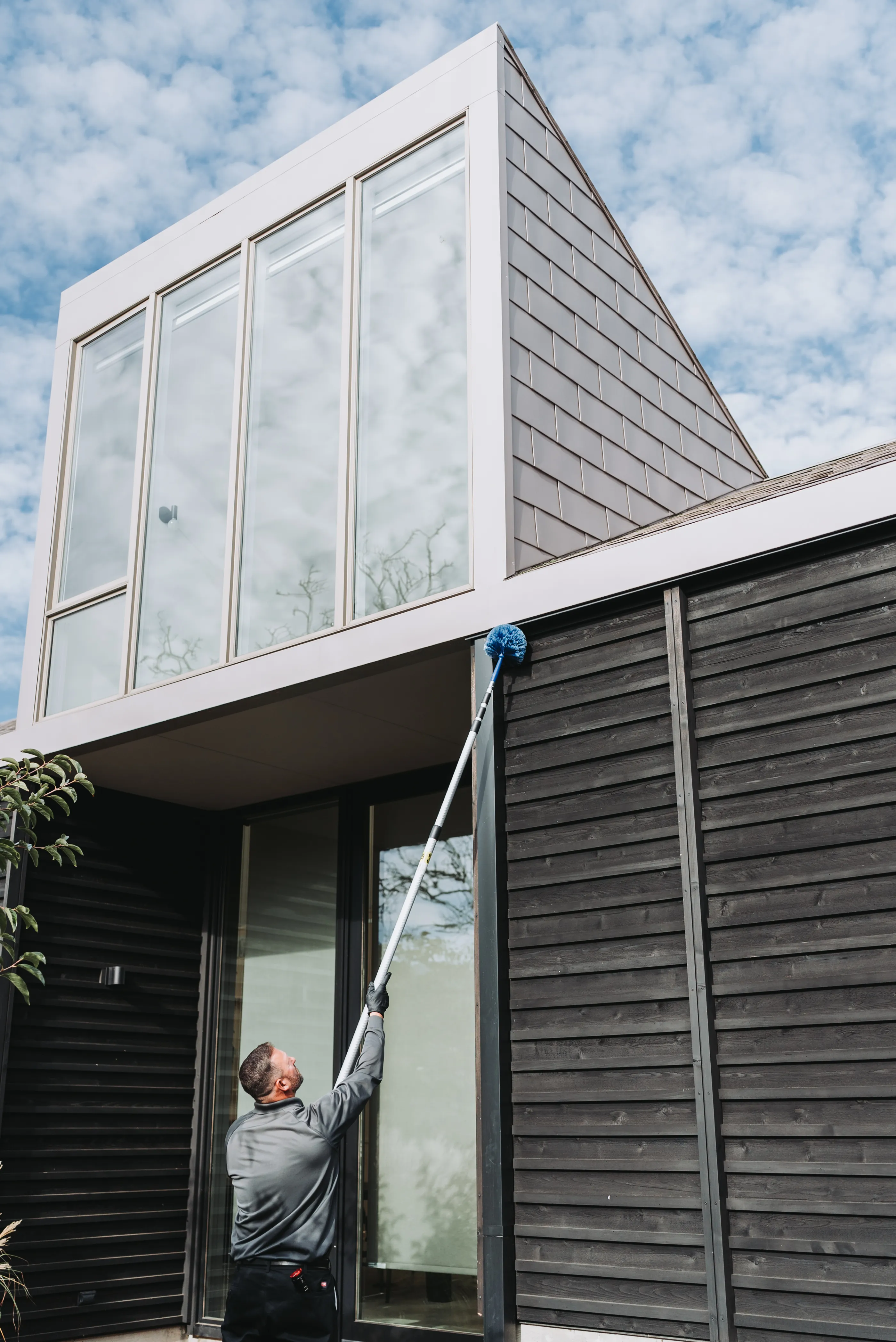 An A&A Pest Control technician removing spider webs from the eaves of a home with an extension pole